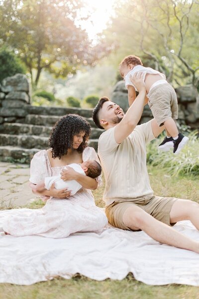 A family sits outside on a blanket together during their NJ newborn photos in a garden.