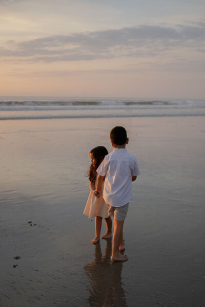Boy and a girl standing at the edge of the water, looking at the waves during sunset