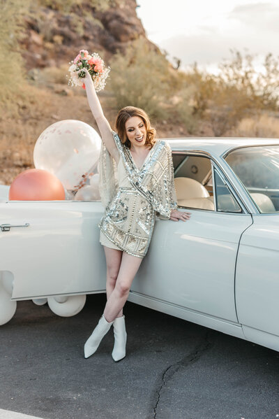 Bride holds bouquet up while leaning on vintage car