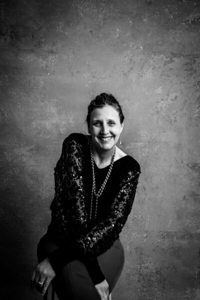 Stylish black-and-white photo of owner Heidi Iliff senior photos Pittsburgh larger than life photography poses on a well lit Gray studio background for a headshot.