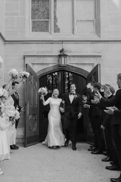 Bride and Groom Walk Through A Tunnel Of Their Friends And Family As They Exit A Church