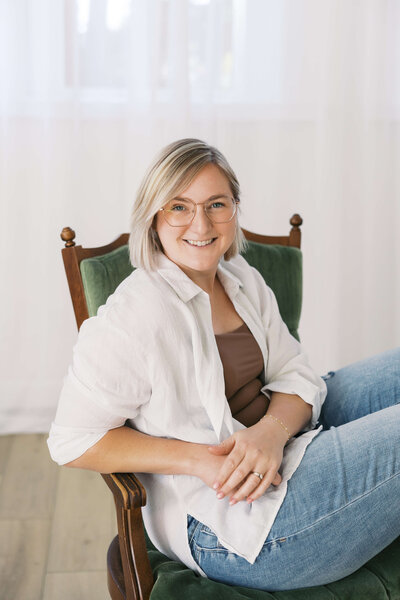 Woman wearing white blouse and jeans sitting on vintage green chair