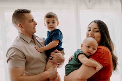 Studio family session with family of four standing in front of white curtain.