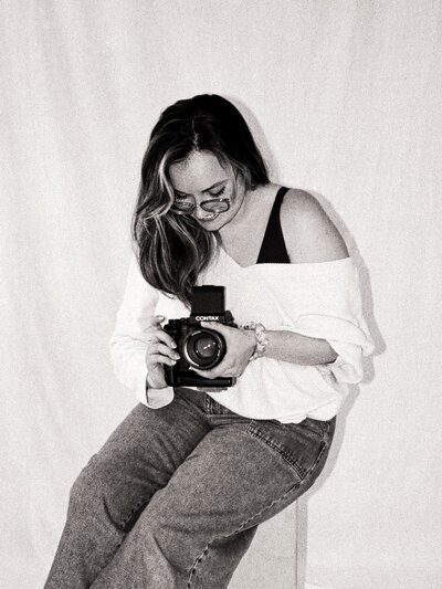 Black and white film portrait of Dominique, seated and looking down while holding a Contax camera — co-founder and film wedding photographer at Castillo Holliday Photo + Film.