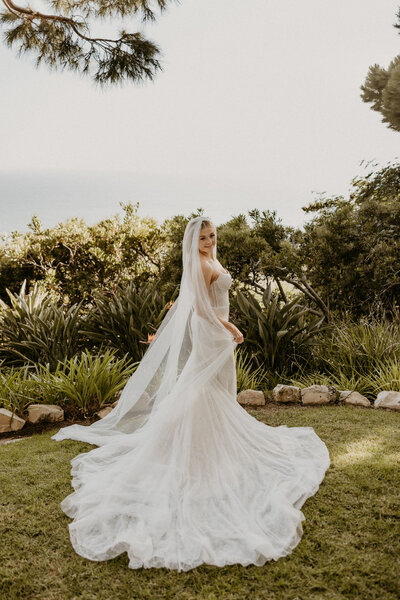 Bride in a flowing gown with long veil posing in a garden setting, planned by Southern California wedding planner Beyond the Event.