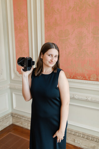 Photographer Hallie captured in a thoughtful pose, dressed in a chic black dress, inside a modern art museum in New York City, showcasing her creative spirit and elegance against a backdrop of gallery art, by Hallie Noel Photography.