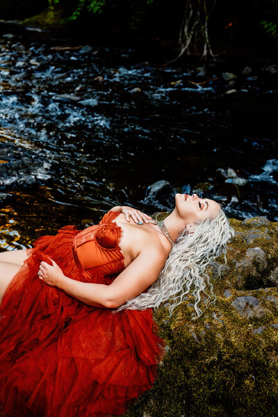 a branding photoshoot for a country artists new single. shes laying on a rock in front of a waterfall