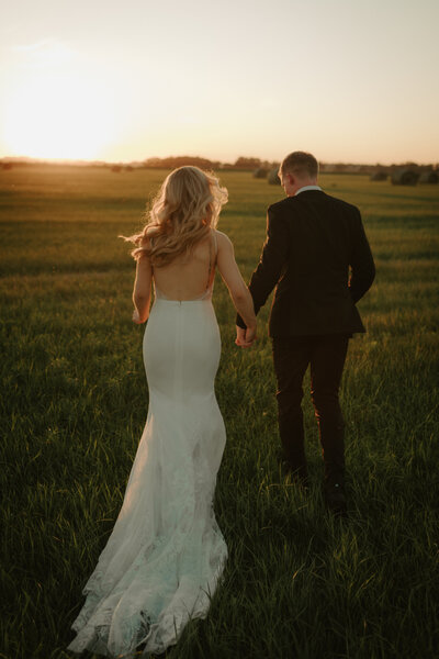 bride and groom holding hands and running into the sunset