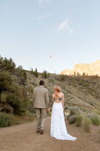 Couple walking on the trail at Smith Rock State Park and looking out at a hot air balloon.