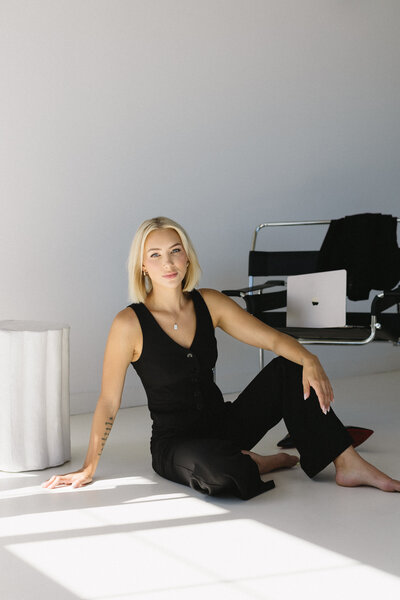 Brand portrait of a realtor wearing a black matching suit, sitting confidently on the floor, showcasing professionalism with a modern twist