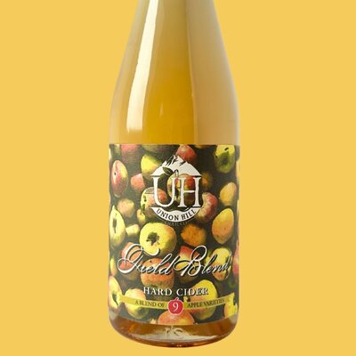 A bottle of Field Blend hard cider made by Union Hill. Label has a bunch of red and yellow apples as the background.