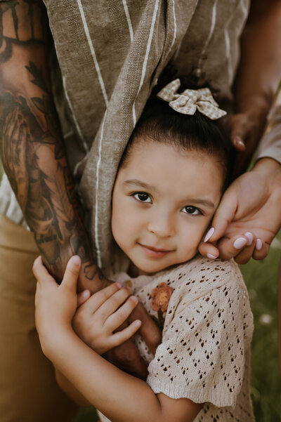 mom hugging a smiling little girl from behind while her some watches over her shoulder on a country road in decatur, tx
