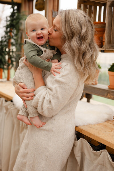 Mom kissing her baby during a family Christmas session, surrounded by holiday decor. 