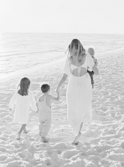 A mom walks on the beach in Santa Rosa Florida holding a baby and the hands of her children