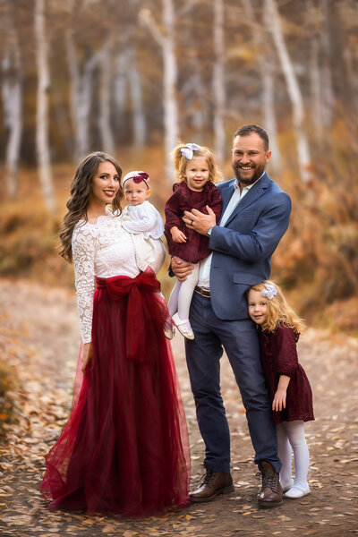 Fine-art family portrait captured by Amber Damour Photography in Kaufman, Texas — featuring parents and three young daughters in coordinated burgundy and white outfits.