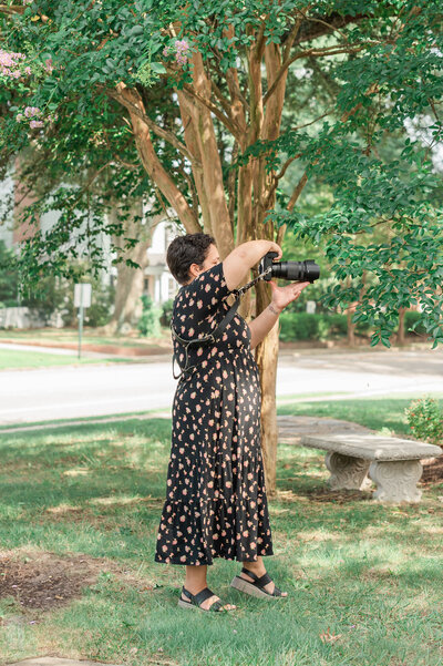 A photographer holding a camera up to take a photo while standing outside