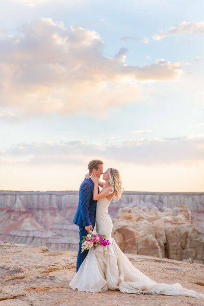 Groom and bride hugging each other at the grand canyon as groom holds the bouquet and sun sets behind them. Taken by Lexington kentucky wedding photographer.