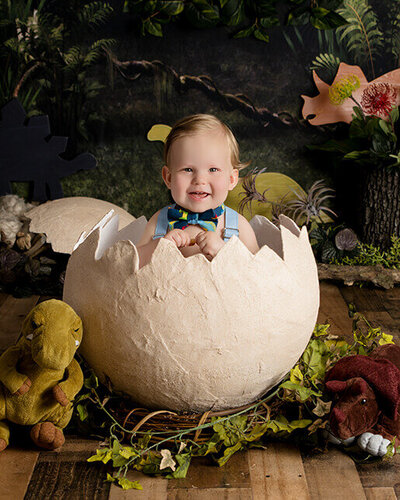 One year old boy smiles while sitting in a dinosaur egg.
