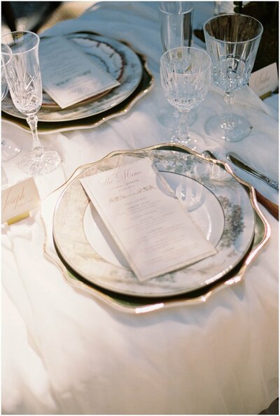 Table setting details with ornate plate and menu with crystal glasses