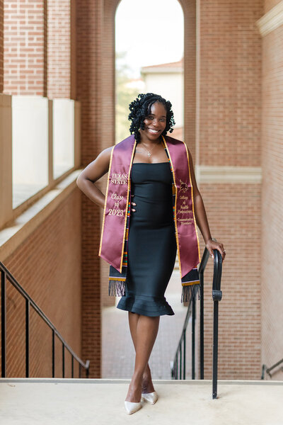 Texas State graduate posing in black dress with graduation stole during senior session on campus in San Marcos, Texas.