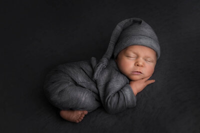 newborn baby boy laying on belly on a beanbag. Beanbag pose. Newborn baby is dressed in gray with a gray sleepy hat on a gray beanbag blanket.