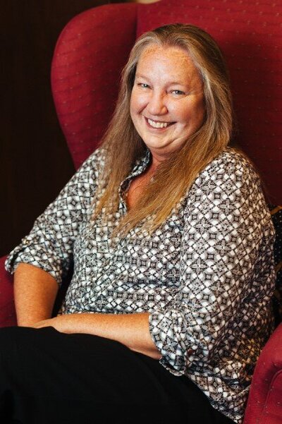 Headshot of Debbie Perry posing on a red wingback chair