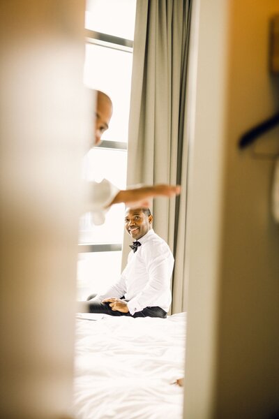 A groomsmen opens the door and waves a the photographer as the groom prepares for the first look.