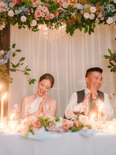 A bride and groom smile surrounded by flower arrangements at Restaurant Richmond.