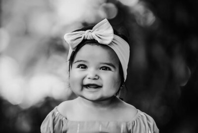 A joyful baby girl smiles brightly, captured in a charming black and white photograph.