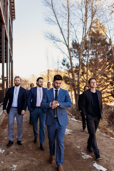 Groom and groomsmen walk down snowy path behind surf hotel in Buena Vista colorado
