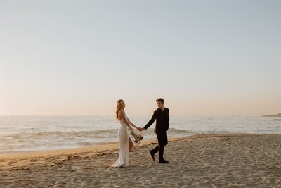bride and groom walking hand in hand at sunset on a beach