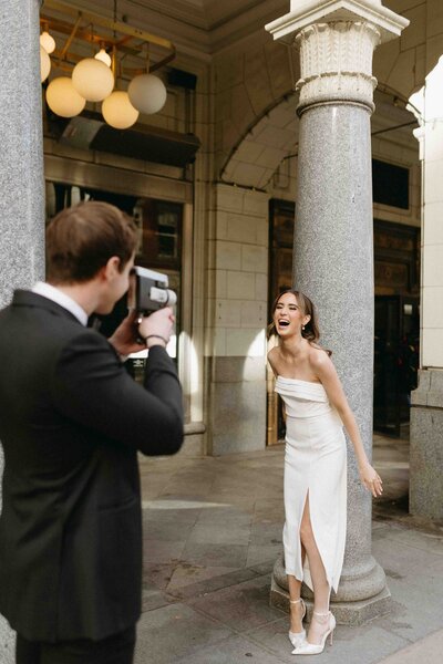 A bride posing for her groom holding a super 8 video recorder.