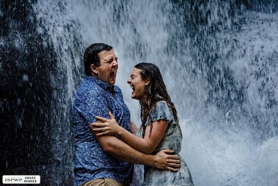 Couple laughs under waterfall in engagement photo by Bobbi Barbarich