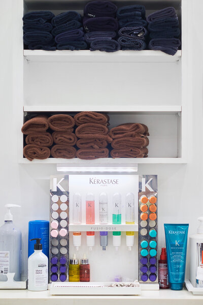 Branding photo of luxury hair care display featuring Kérastase products and folded salon towels at Denise Antonacci Salon in Charlotte, NC. Captured by DeLong Photography to showcase high-end salon organization, professional styling products, and clean aesthetic for beauty industry branding.
