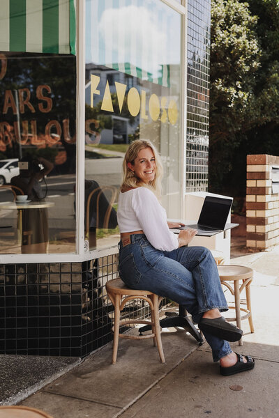 Woman sitting in front of a cafe, working on her laptop