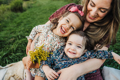mom holds toddler daughters on lap and everyone laughs for a picture
