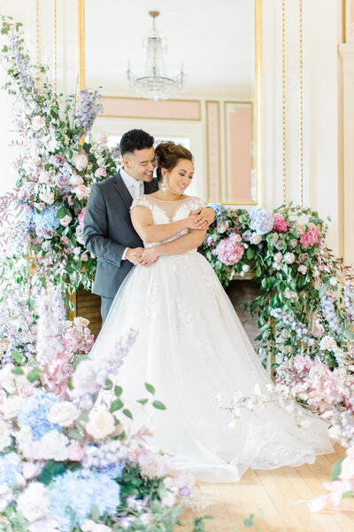 Bride and groom posing in the middle of large floral arrangements and greenery