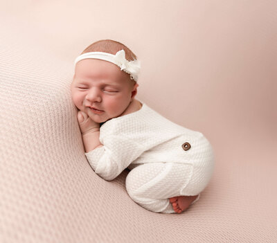 Newborn photo of a baby girl in bum up pose on a pink background