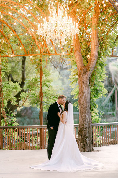 bride and groom facing eachother standing in a walkway under a canopy of trees with beautiful backlight at spanish hills club in camarillo, ca taken by magnolia west photography