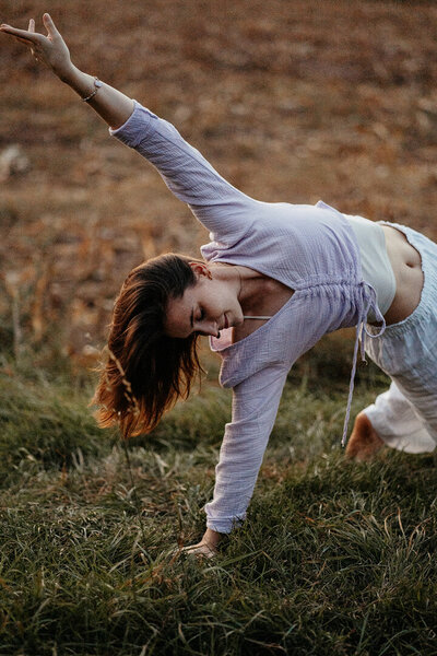 Tessa Adrian in einer Yoga-Pose auf einem Feld, Natur im Hintergrund.
