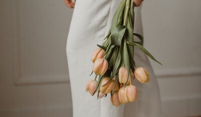 Close-up of a woman holding a bouquet of peach-colored tulips against a soft beige backdrop.