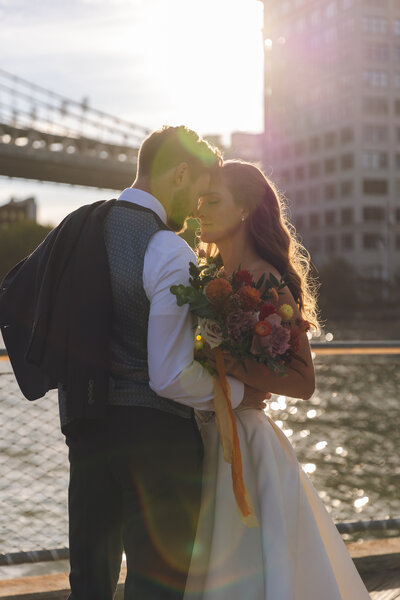 Bride and Groom embracing at golden hour with Brooklyn bridge behind them