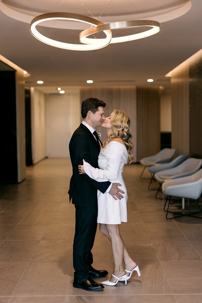 Bride and groom share a kiss inside Brisbane Registry Office under modern circular light fitting