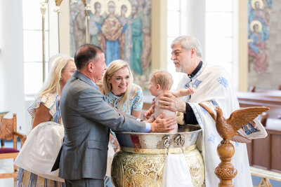 Couple and priest holding a baby being baptized in a church.