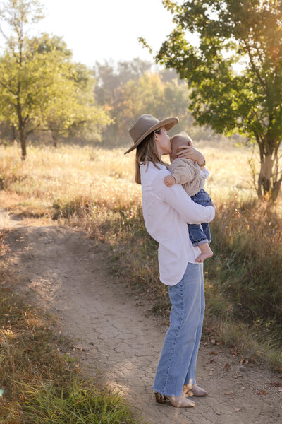 Mother gently kissing her baby son's head as she snuggles him. Candid, lifestyle, motherhood photography in Minnesota