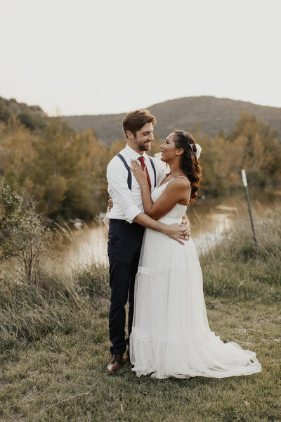 A bride and groom share a romantic moment outdoors in the Texas Hill Country during their wedding in Leakey, Texas, surrounded by soft hills and golden light.
