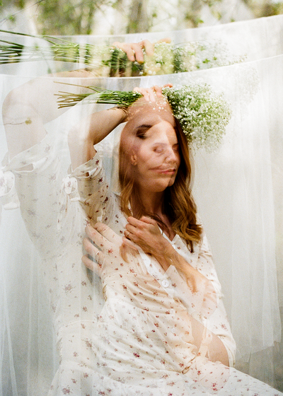 a double exposure of a woman holding flowers her head while her hand rests on her chest