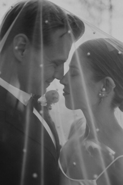 A black and white photo of a couple face to face under a wedding veil.