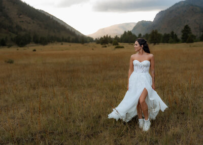 Bride in a strapless wedding gown standing in a golden field with mountains