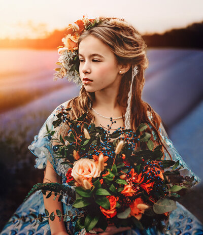 ung girl with red hair in a braided crown in a blue dress in a field